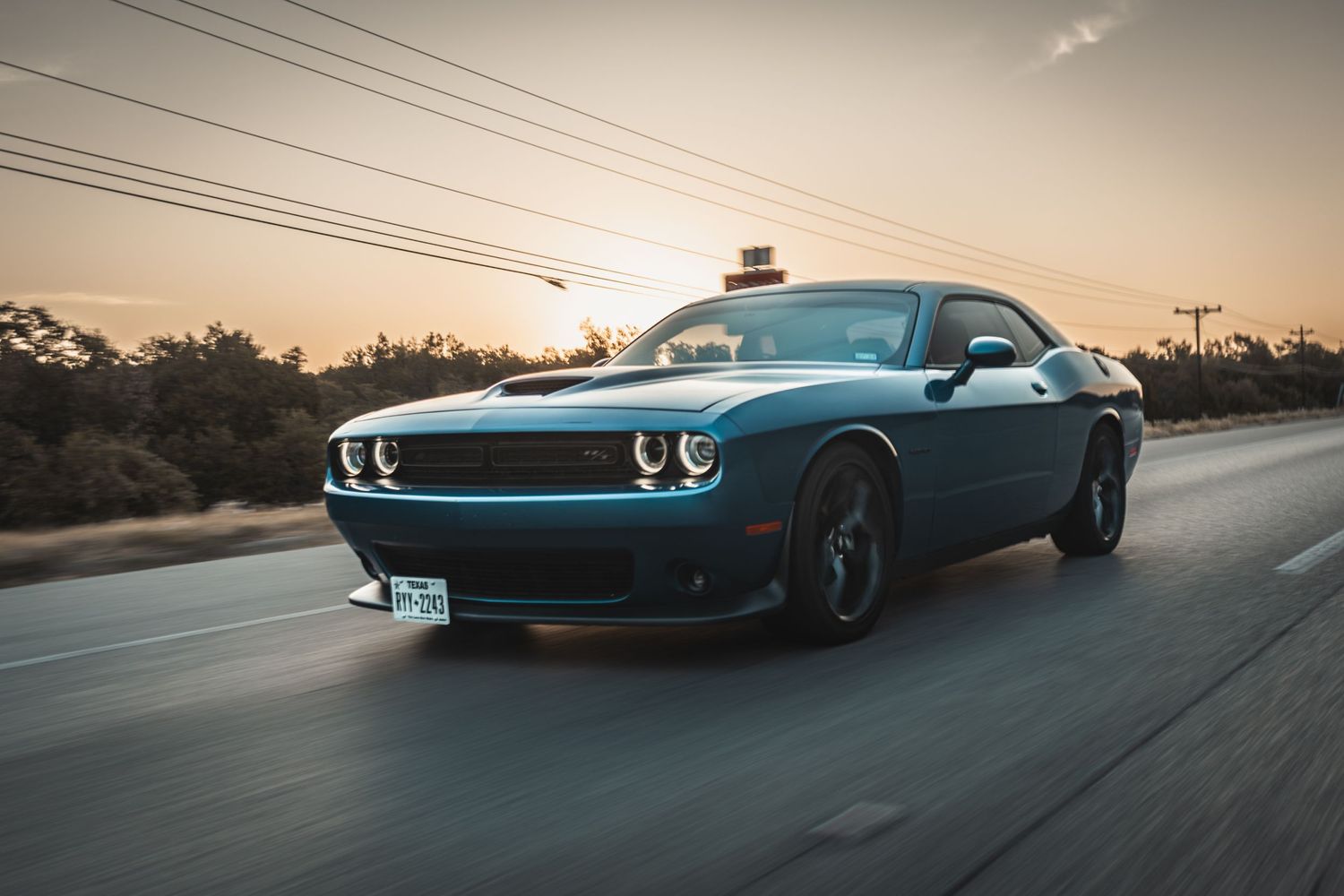 Blue Dodge Challenger with retro-styled front end cruising at sunset.