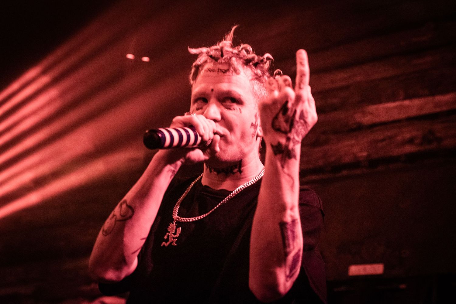 Performer in black tank top singing on stage with dramatic red lighting.