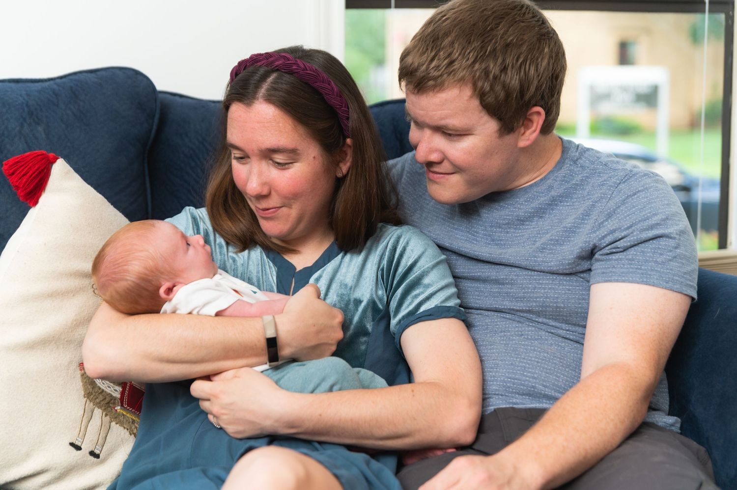 Parents in casual attire snuggle with infant on blue couch.