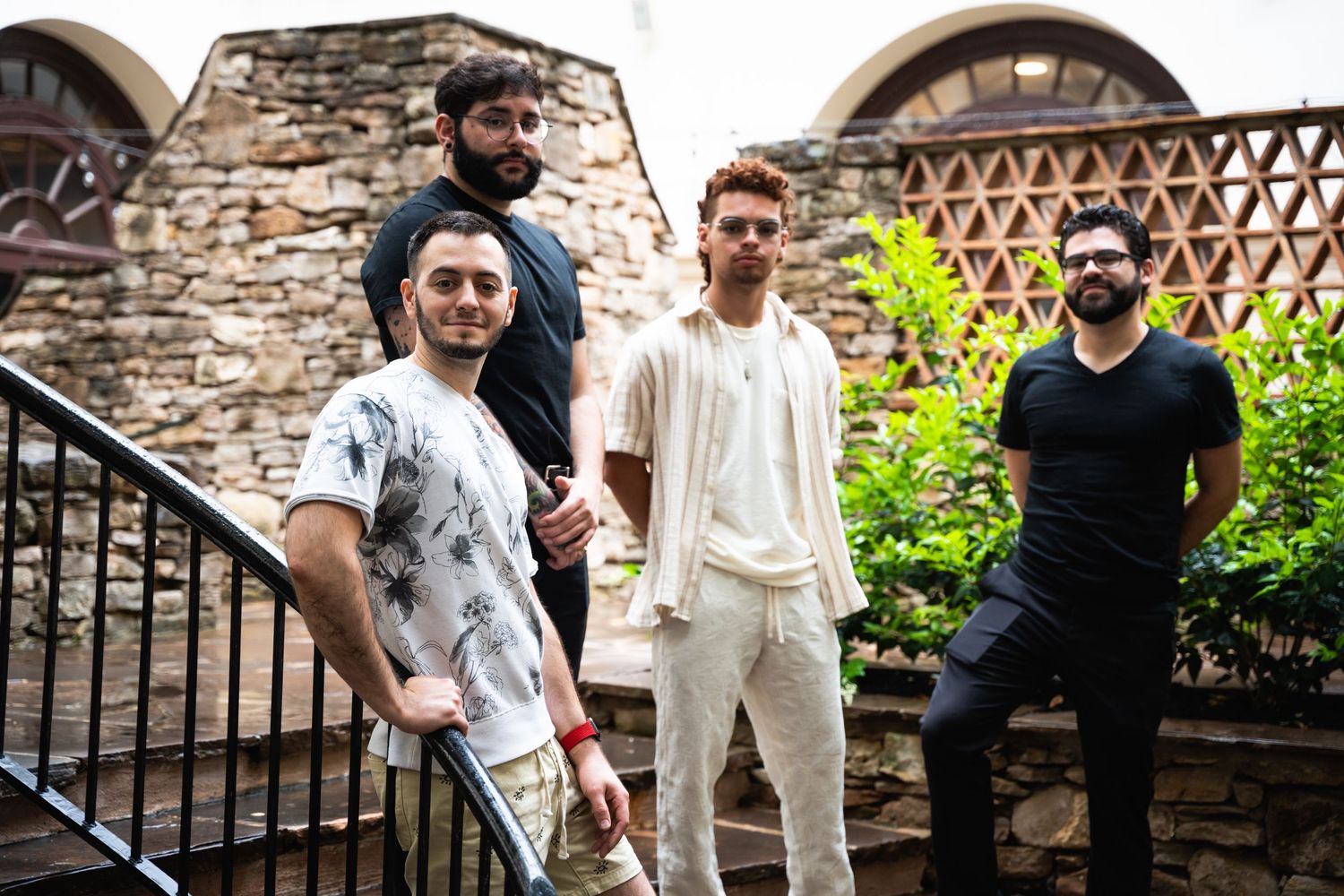Band members pose on stone steps in an outdoor setting with architectural details in the background.