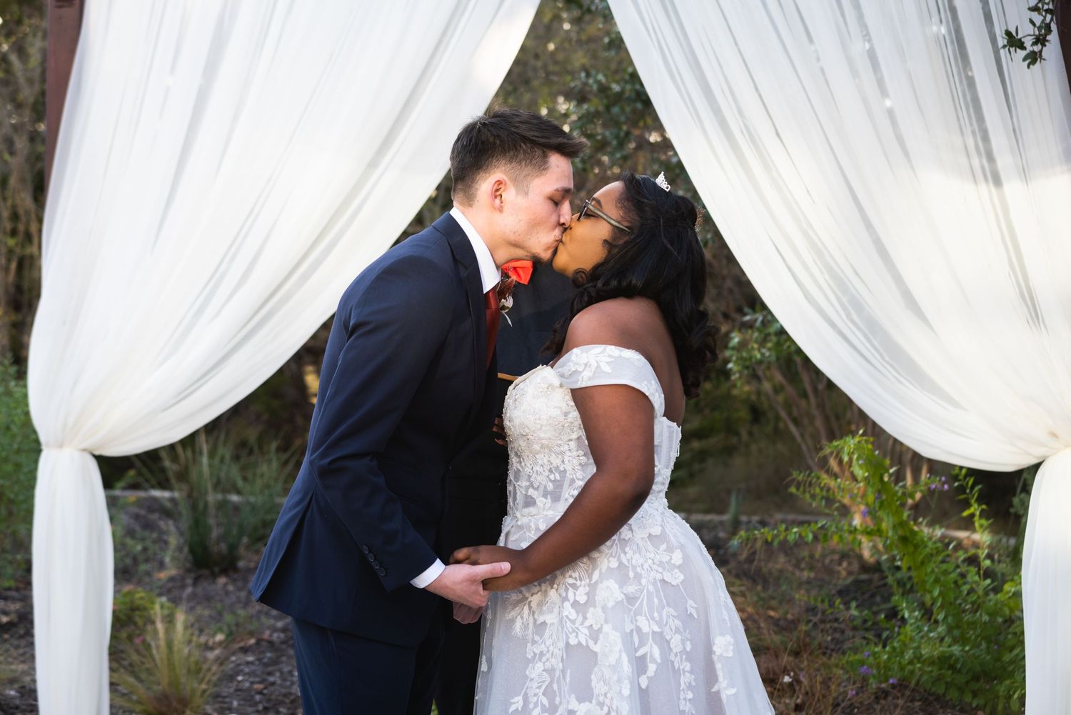 A romantic kiss between newlyweds under flowing white fabric drapes at their outdoor ceremony.