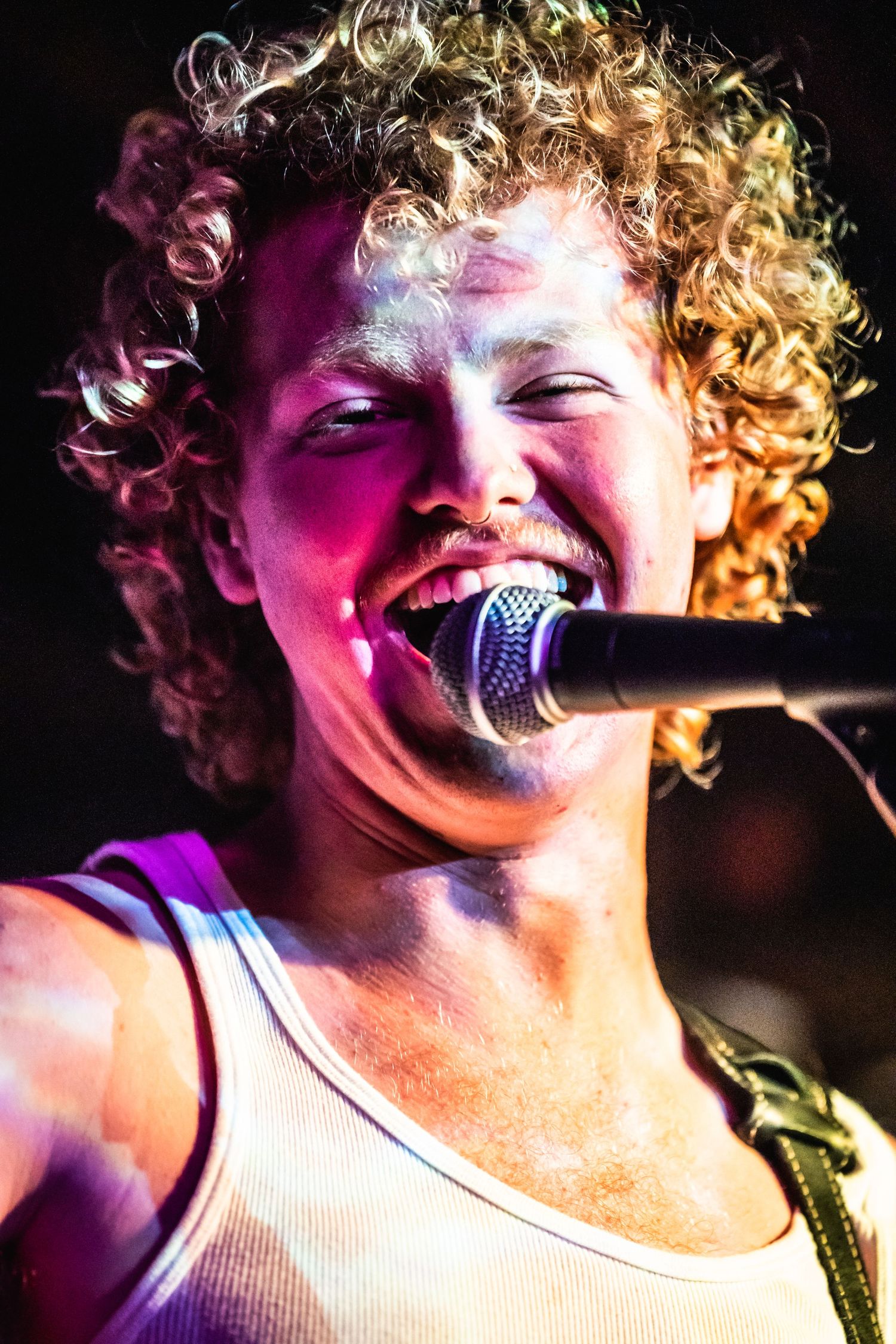 Performer singing passionately into microphone under colorful stage lighting.