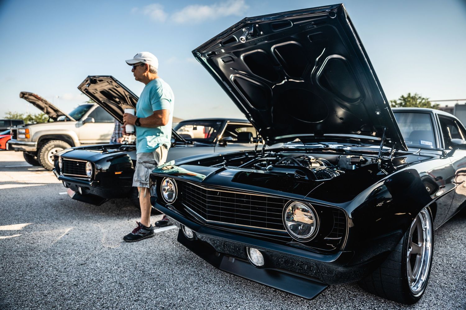 Classic black muscle car with hood open at a car show event.