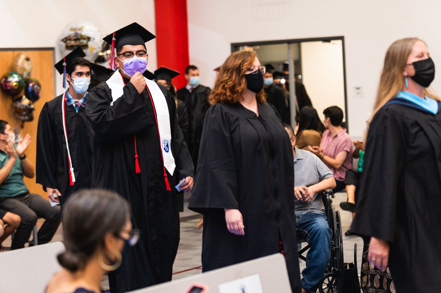 Graduates wearing protective masks proceed through graduation ceremony.