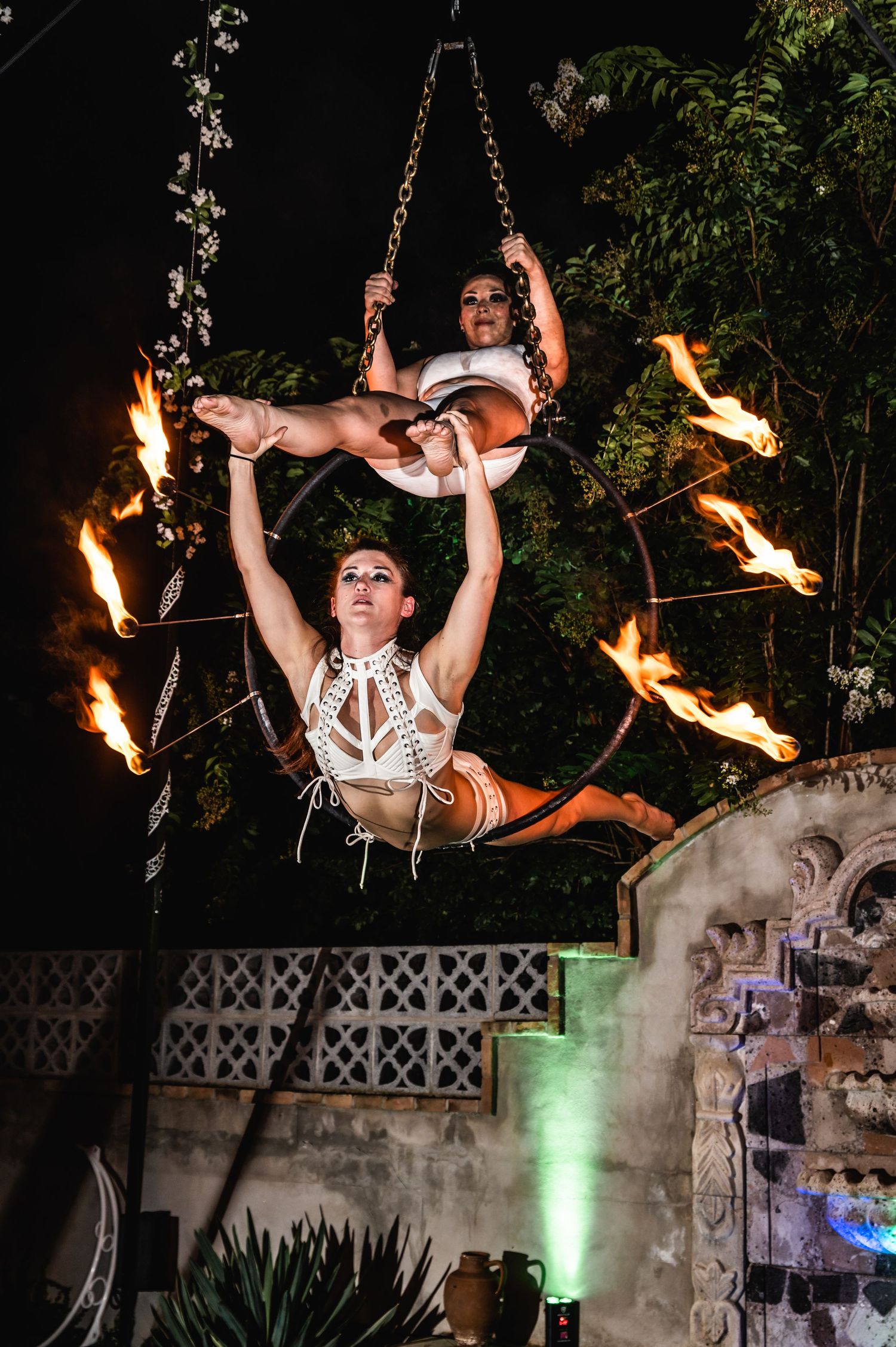 Acrobatic performers execute complex aerial maneuver surrounded by fire torches at night.