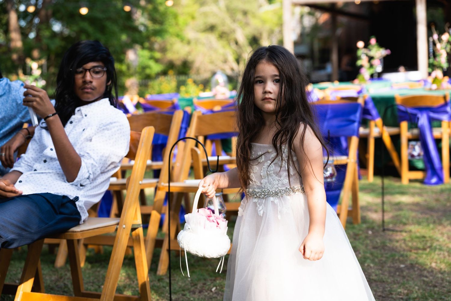 Wedding guests sit in wooden chairs at an outdoor celebration.