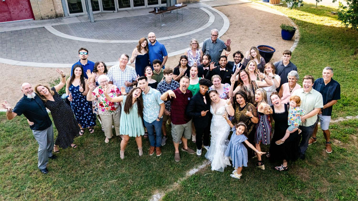 A large group of wedding guests poses together on a grassy slope for a fun photo.