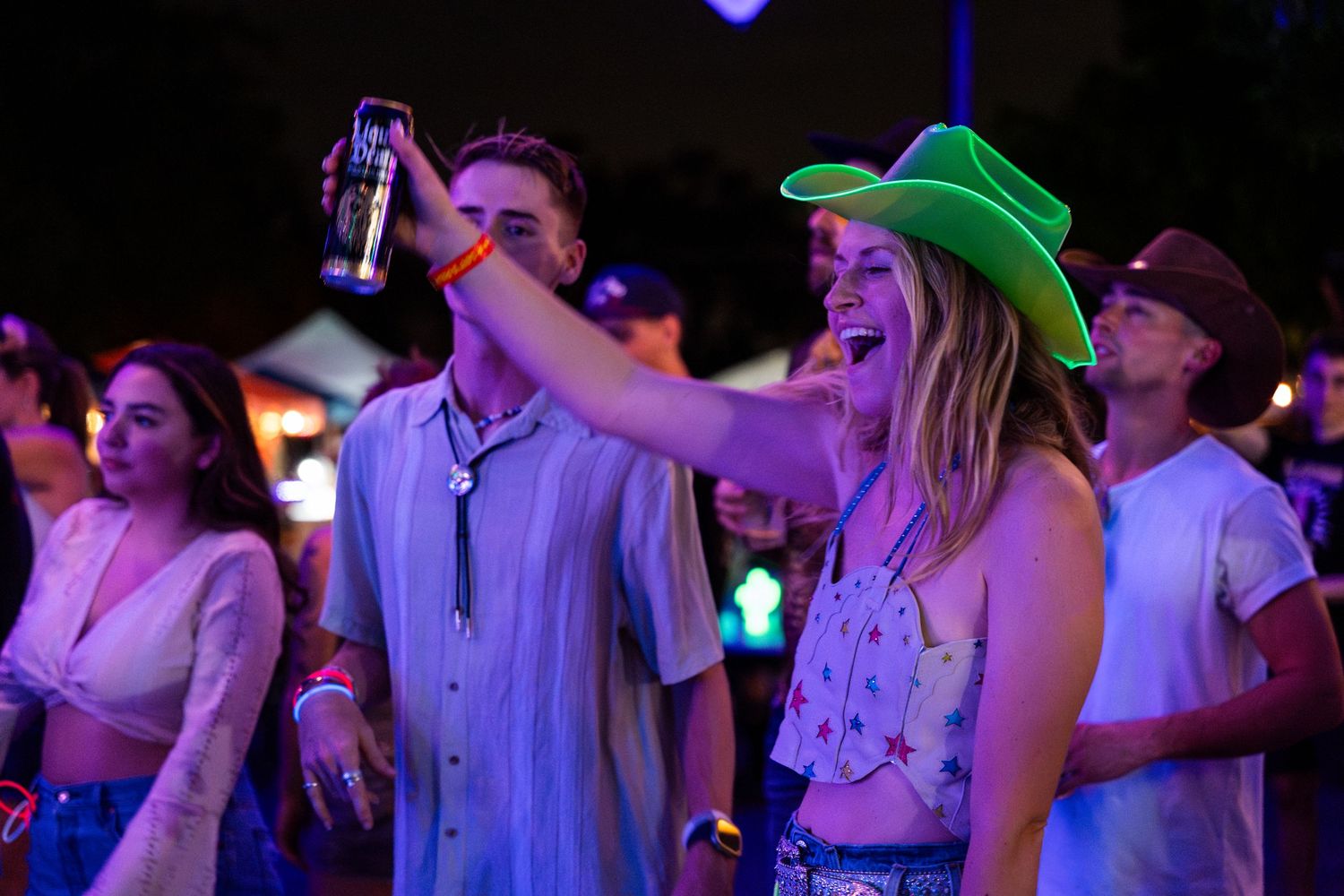 Party crowd dances and celebrates with colored lights illuminating a dark nightclub atmosphere.