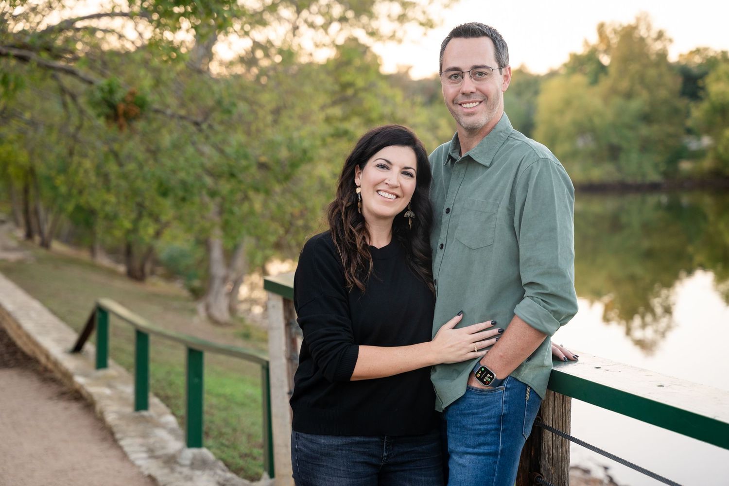 A couple poses along a lakeside path during golden hour.