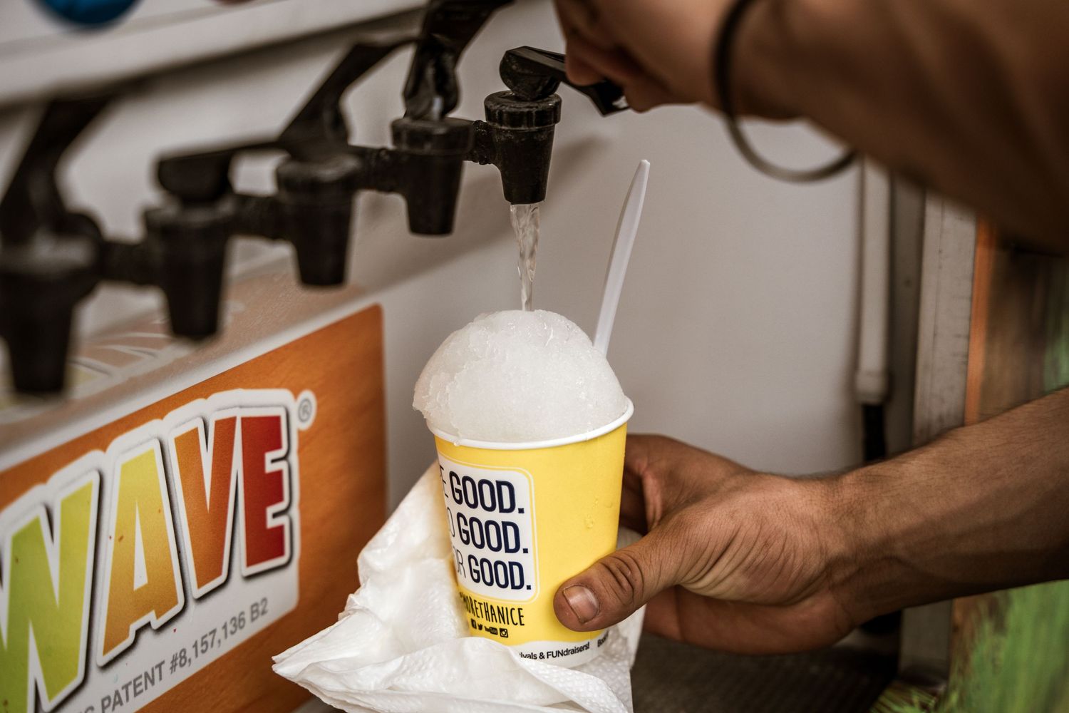Hand dispensing white frozen drink into yellow cup at concession stand.