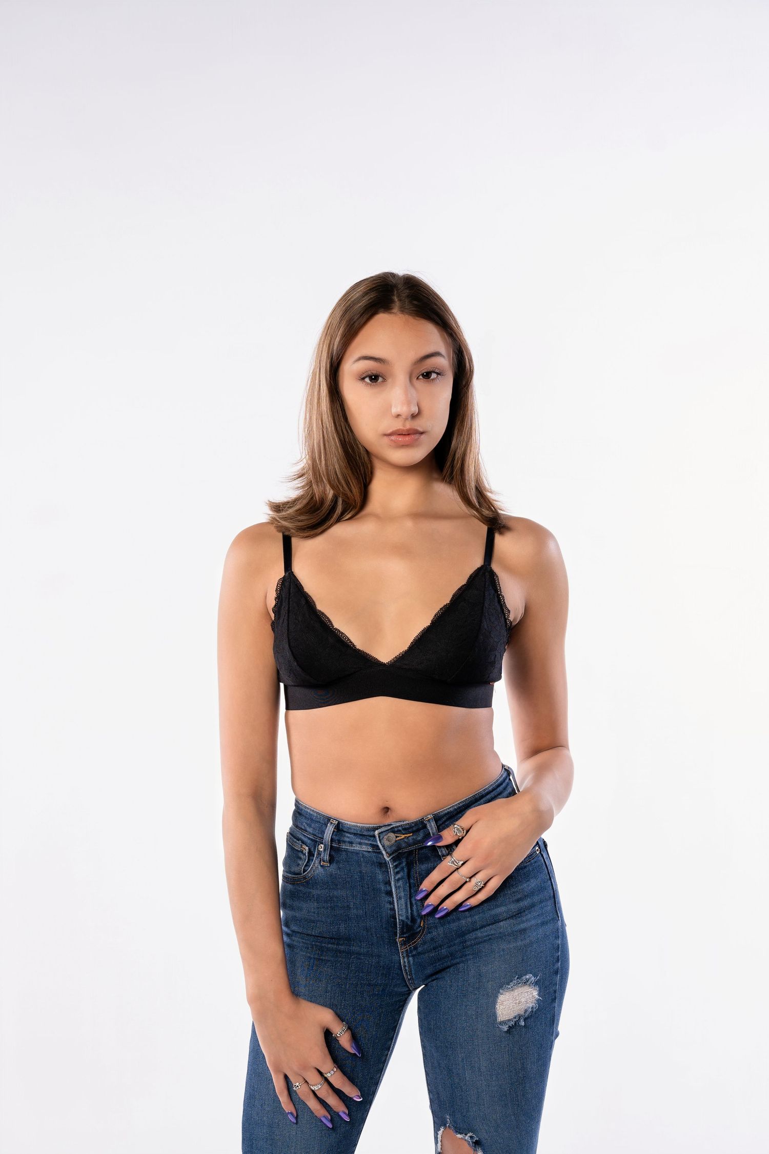 Model in casual outfit with black top and ripped jeans posing against white backdrop.