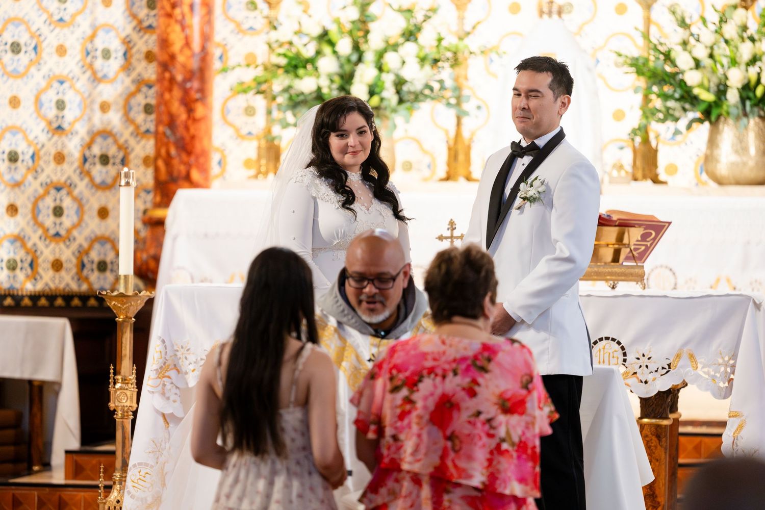 A wedding ceremony takes place in a church with floral decorations and clergy performing the service.