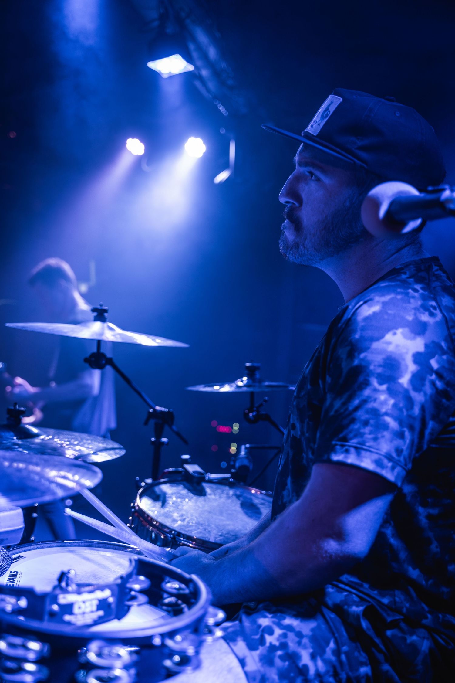 Drummer performing on stage with dramatic blue concert lighting and effects.