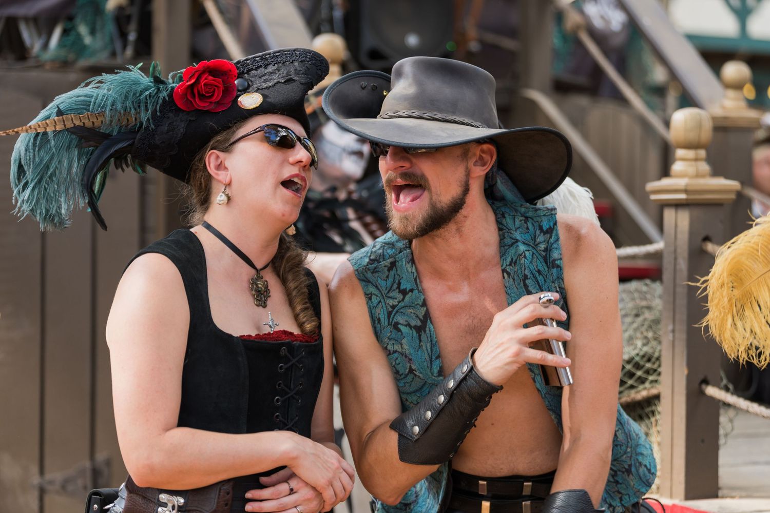 Two festival performers in vintage costumes with feathers share a laugh at a Renaissance fair.