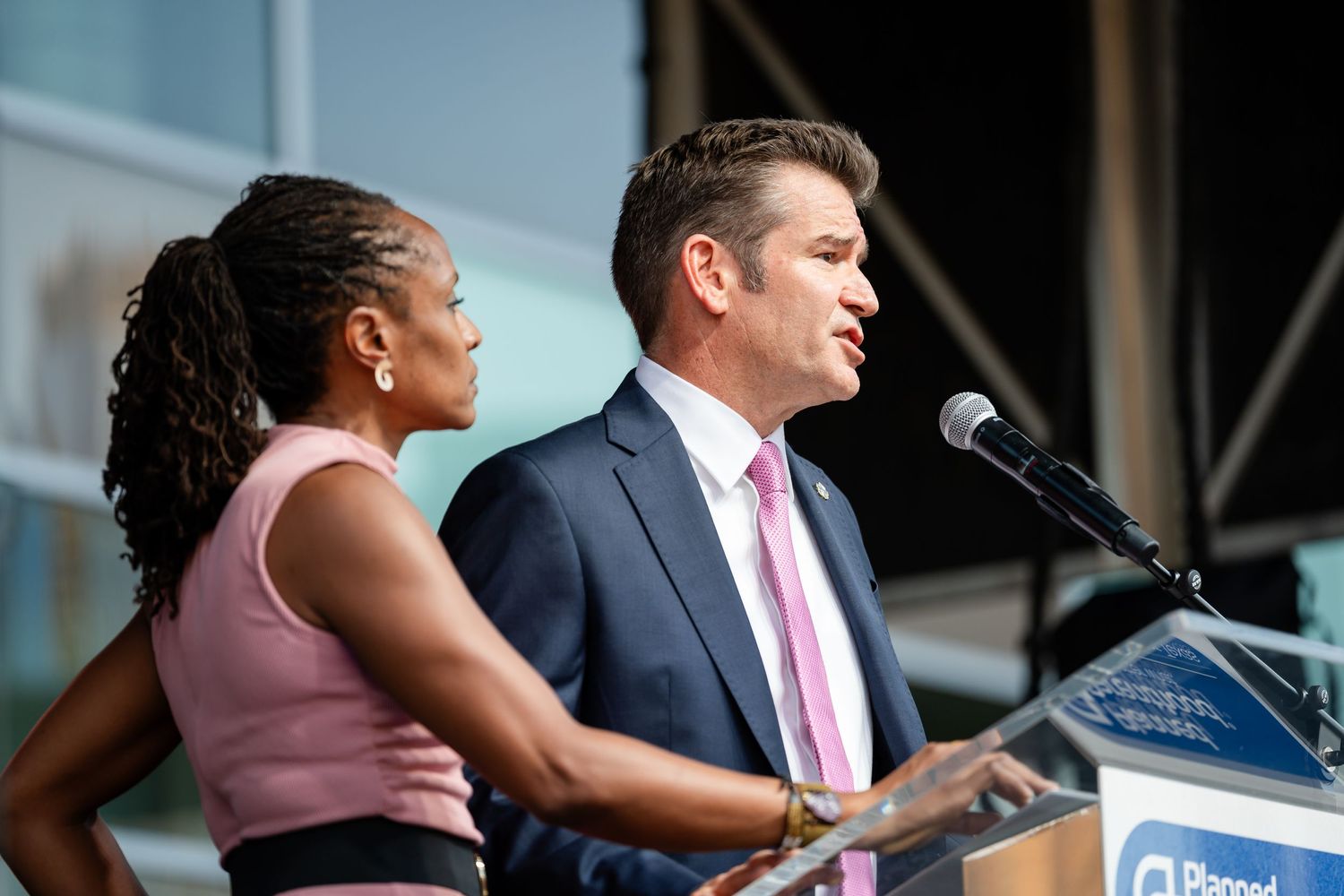 Two speakers sharing podium during outdoor presentation event.