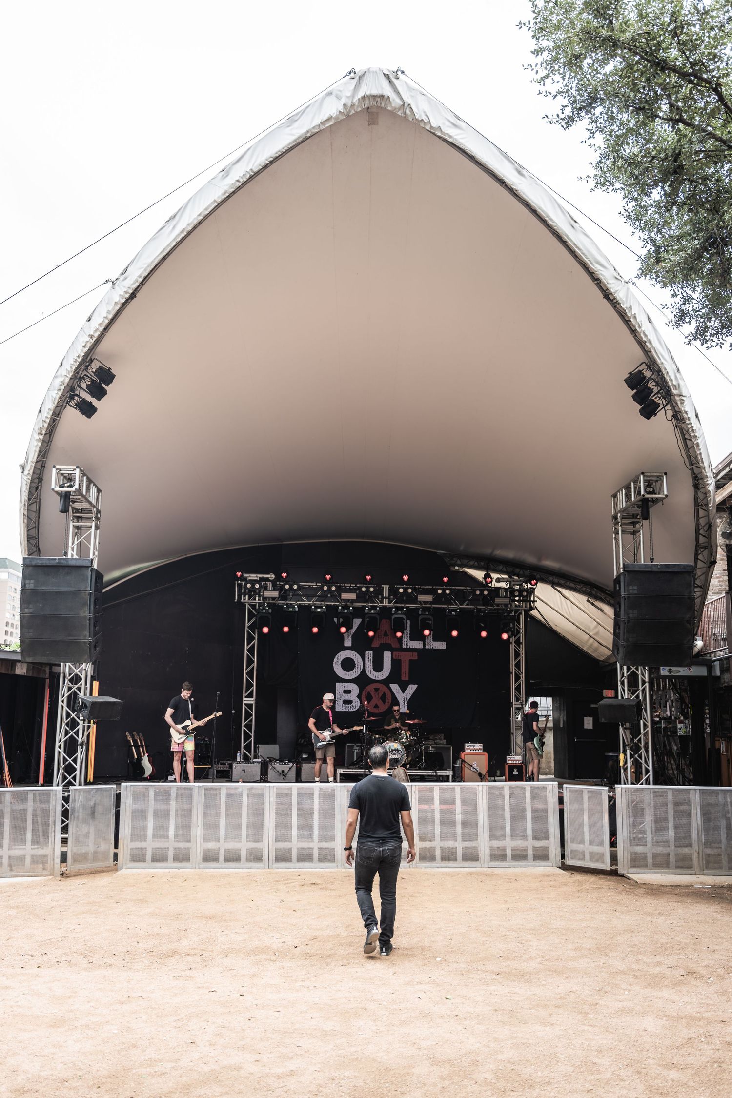 Concert stage setup under large white tent canopy at outdoor music venue.
