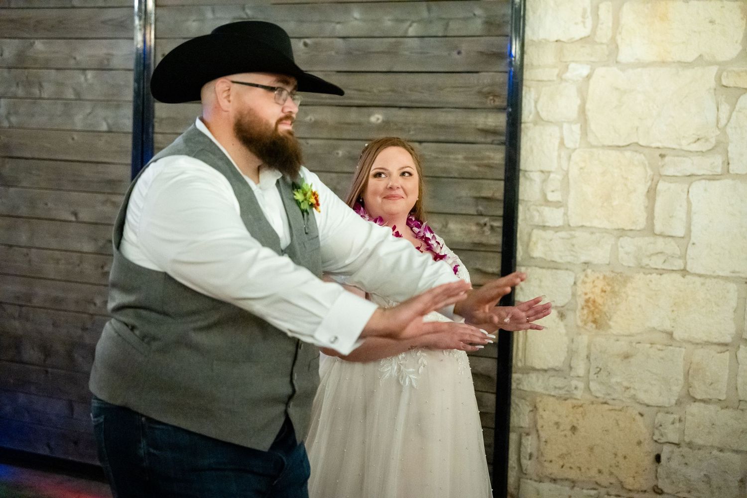 A couple in western attire gesturing during what appears to be a dance instruction at a rustic venue.