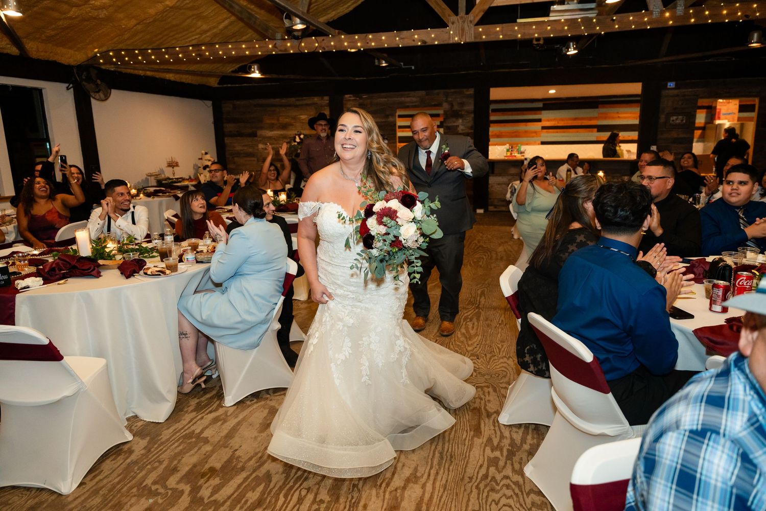 A wedding reception in a rustic venue with wooden floors and white tablecloths as guests celebrate.