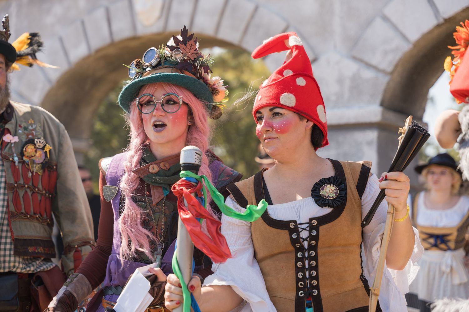 Performers in festive renaissance attire entertain crowds under stone archways at a fair.