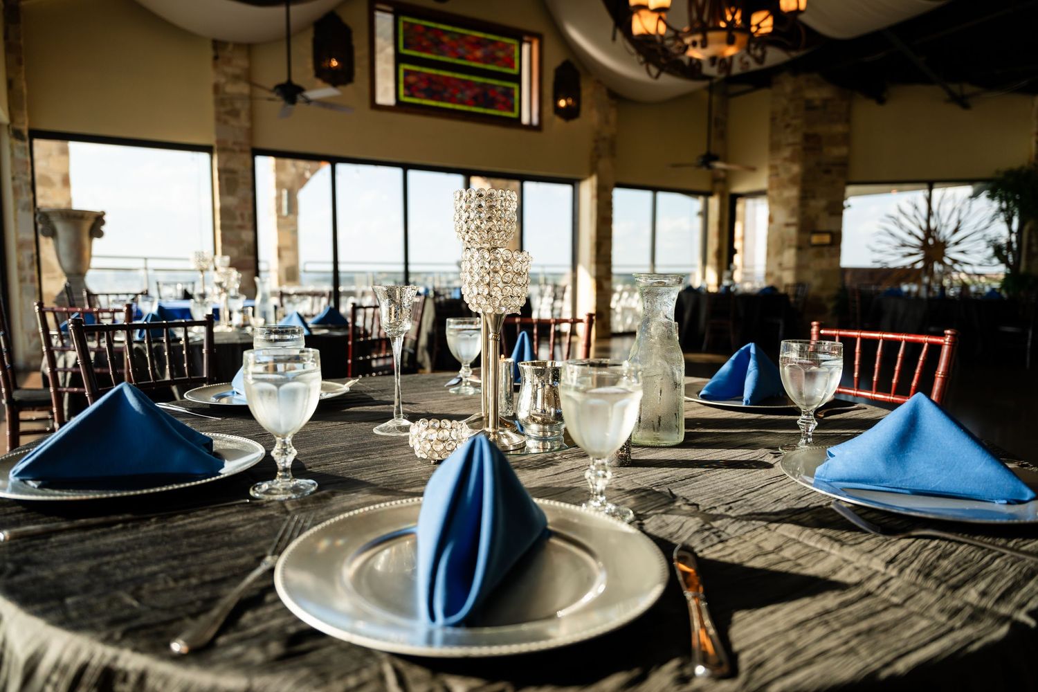 Formal dining table set with blue napkins and white plates in an elegant room with large windows.