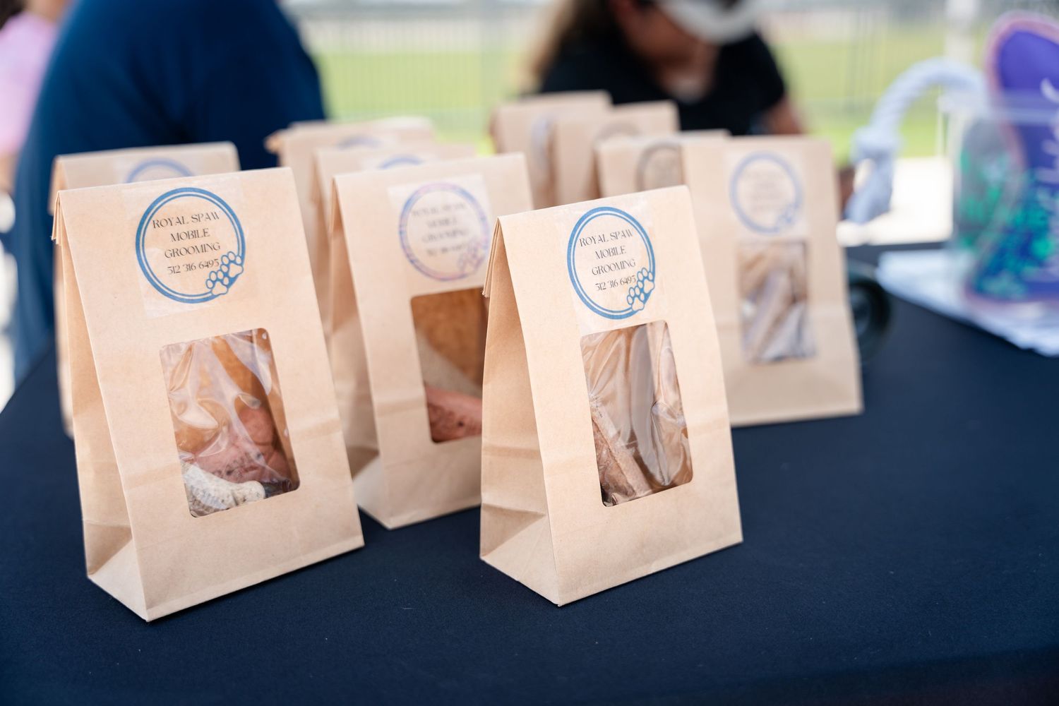 Brown paper bags with clear windows containing treats arranged on a black table at an event.