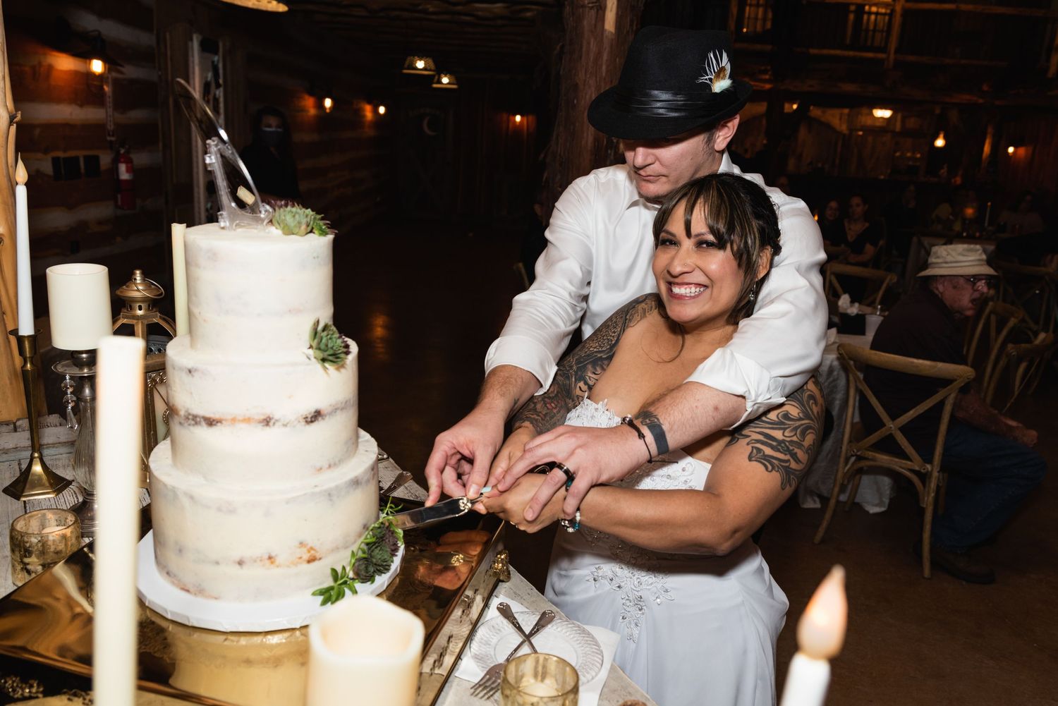 A couple cuts their wedding cake together at a rustic indoor reception.