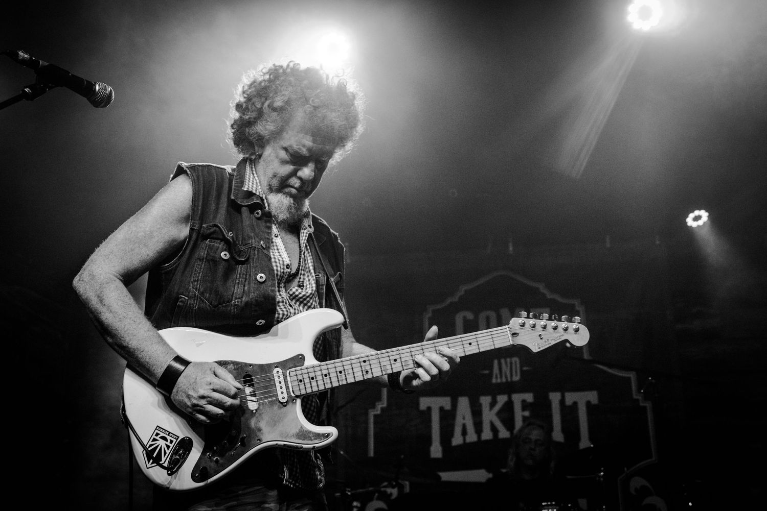 Black and white concert photo of musician playing electric guitar with dramatic spotlights.