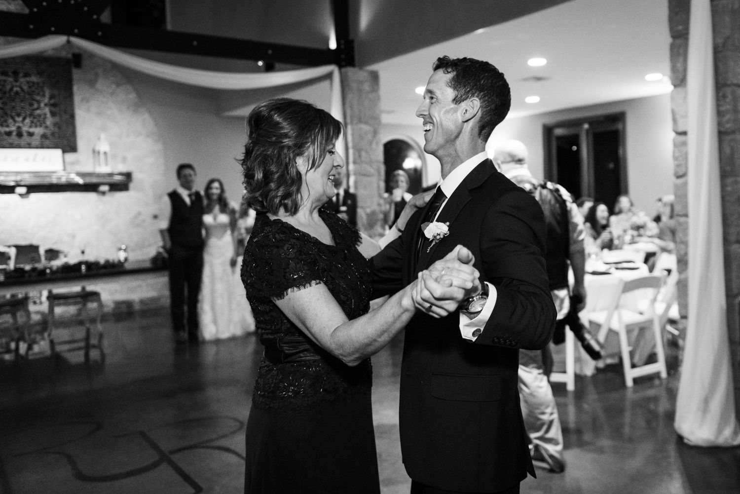 An intimate black and white photograph of a dance at a reception venue.