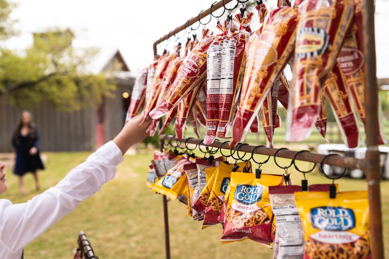 Hand reaching for hanging snack bags at an outdoor concession display.