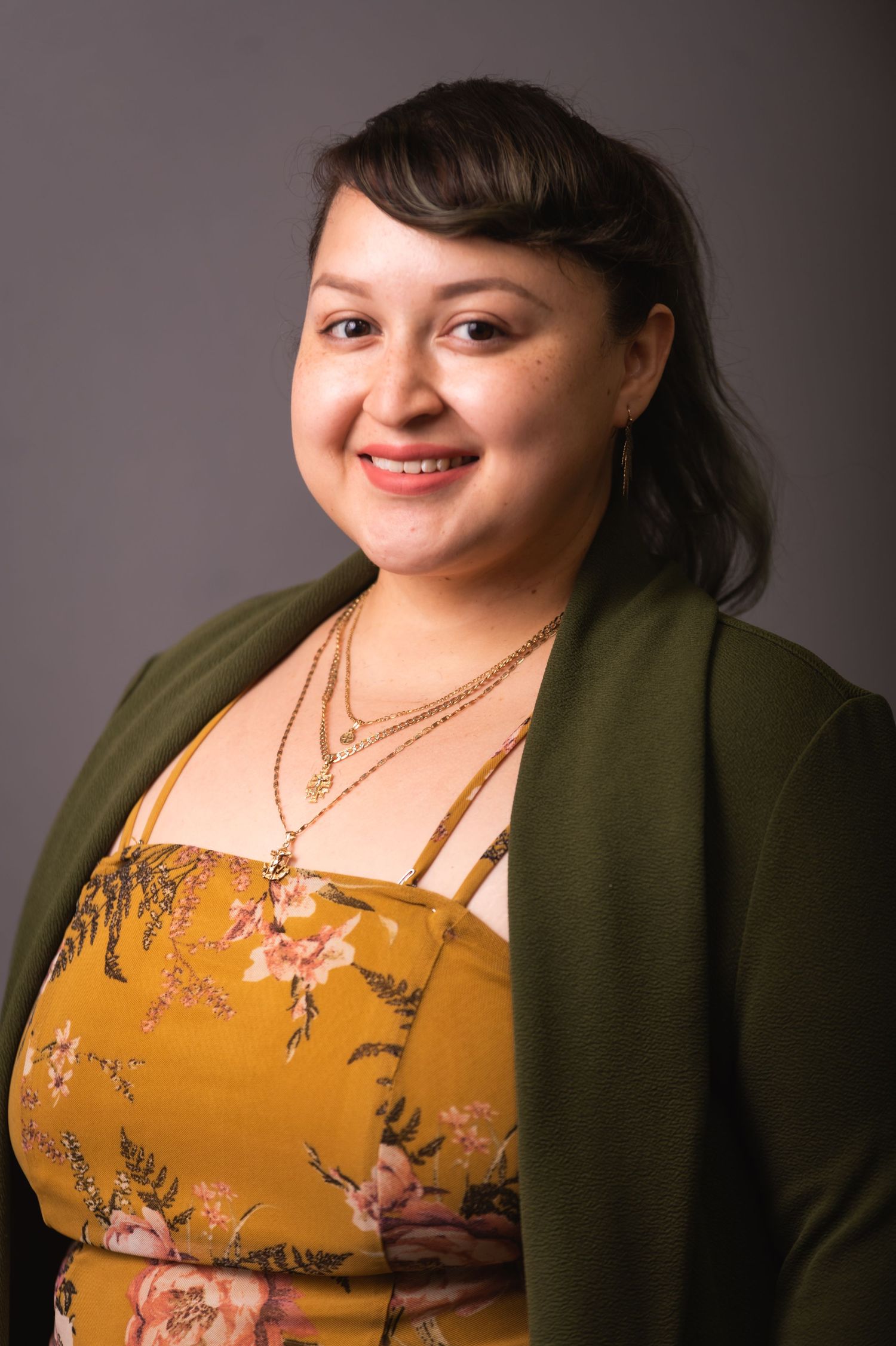 Portrait in studio lighting showing yellow floral top and green cardigan with layered necklaces.