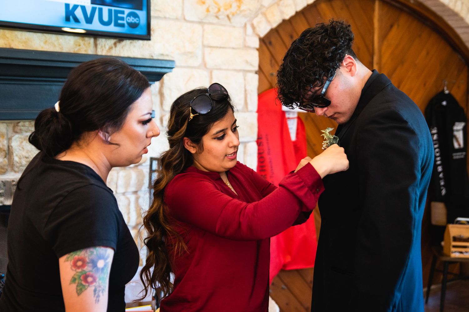 Three people help with formal attire adjustments during a pre-event preparation.