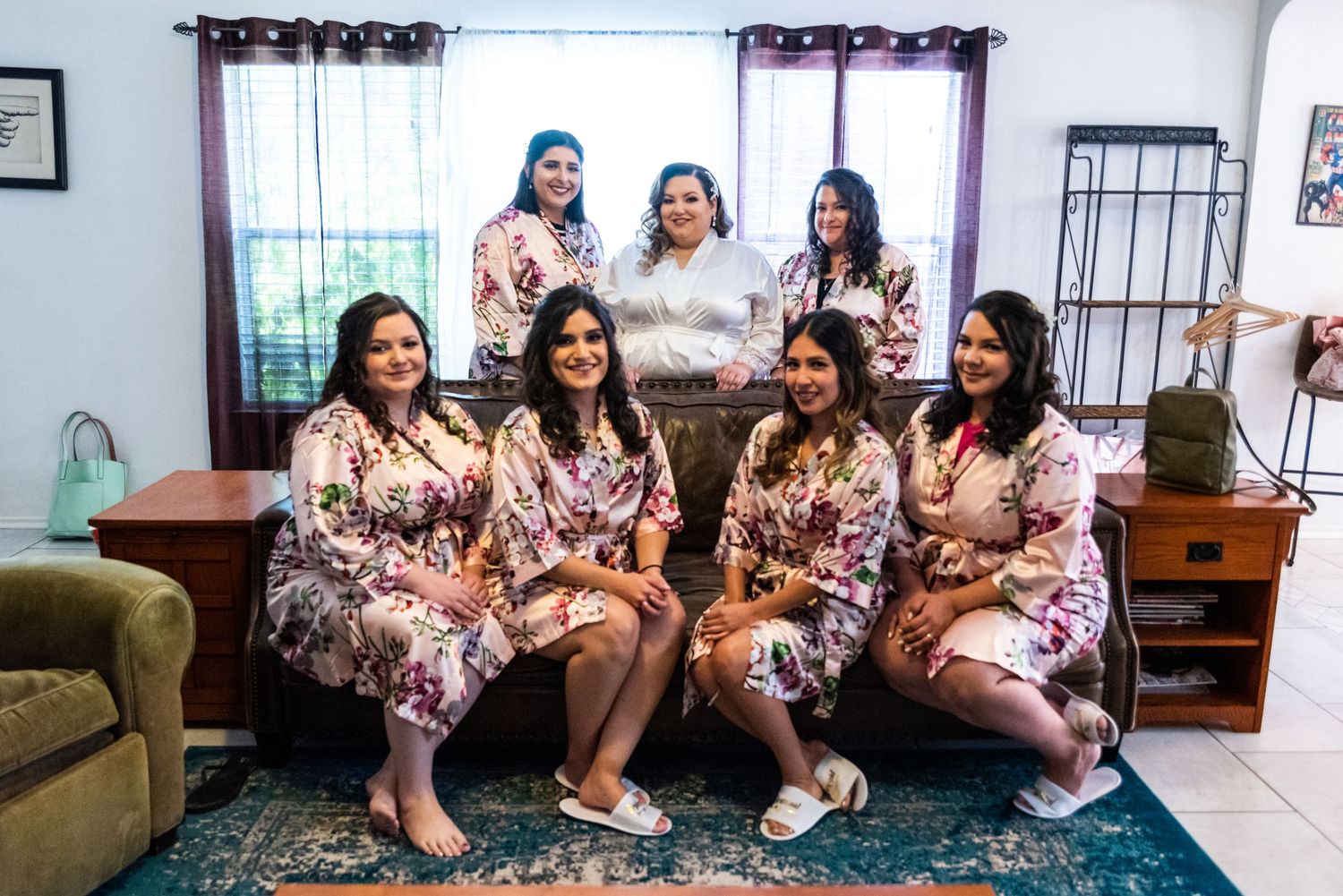 Group photo of bridesmaids wearing matching floral robes sitting together before ceremony.