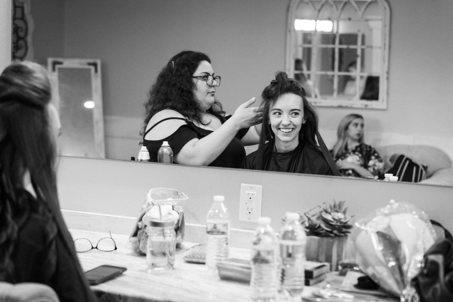 A styling session takes place in a brightly lit dressing room with mirrors and stations.