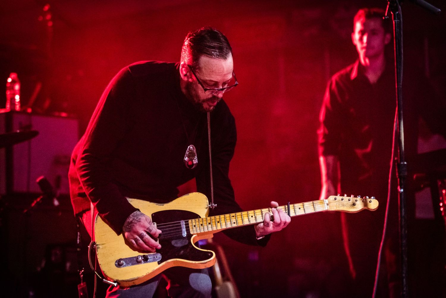Close-up of guitarist playing yellow Telecaster guitar bathed in red stage lighting.