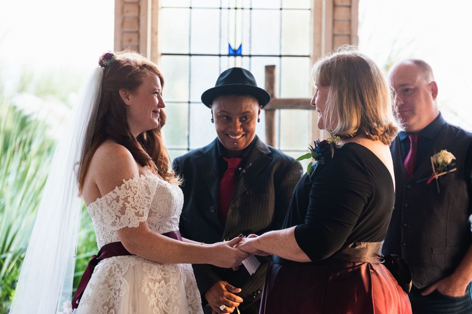 Wedding ceremony taking place in front of a window with palm fronds visible outside.