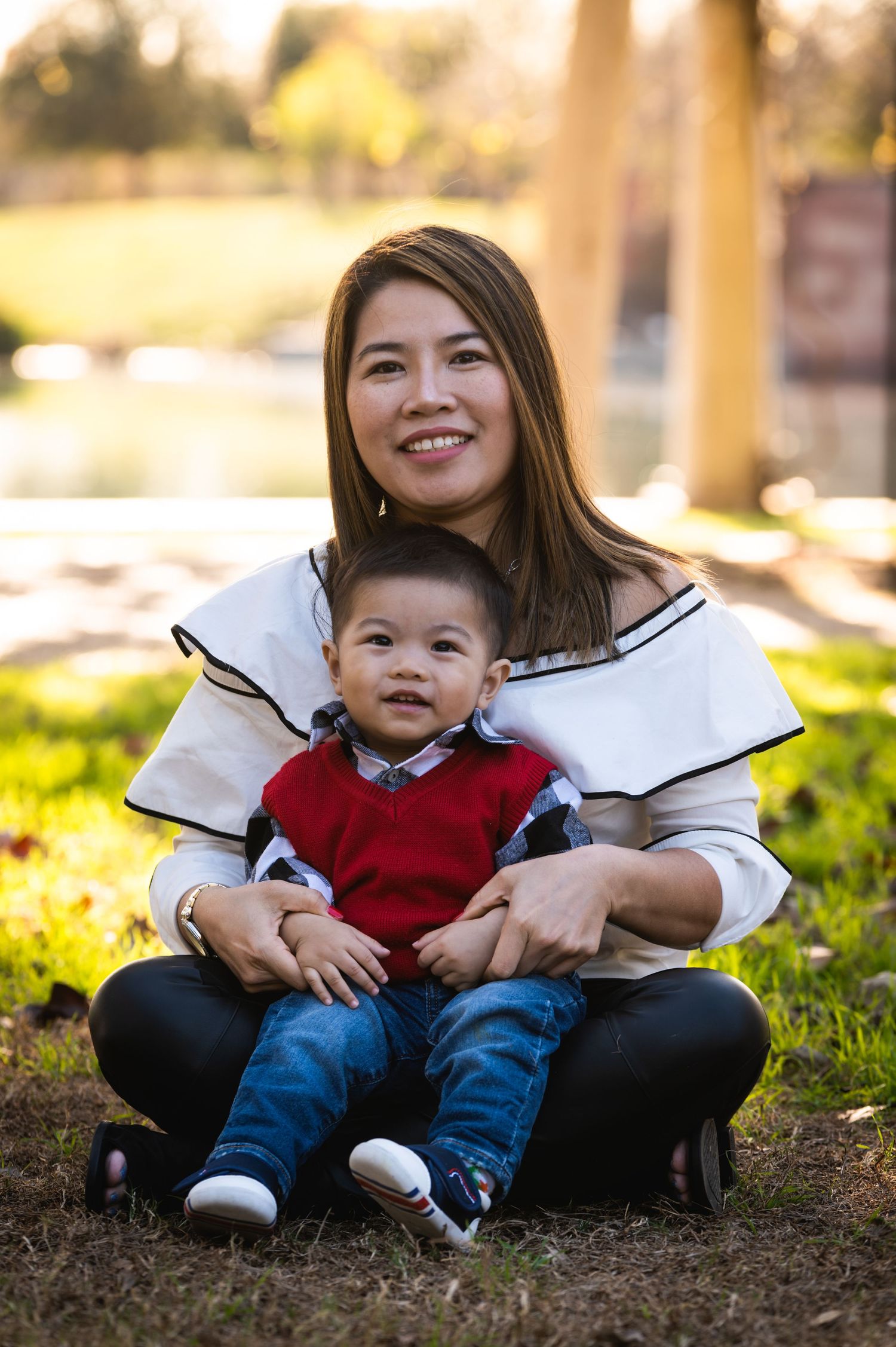 An outdoor portrait of a parent and child sitting together on grass in warm sunlight.