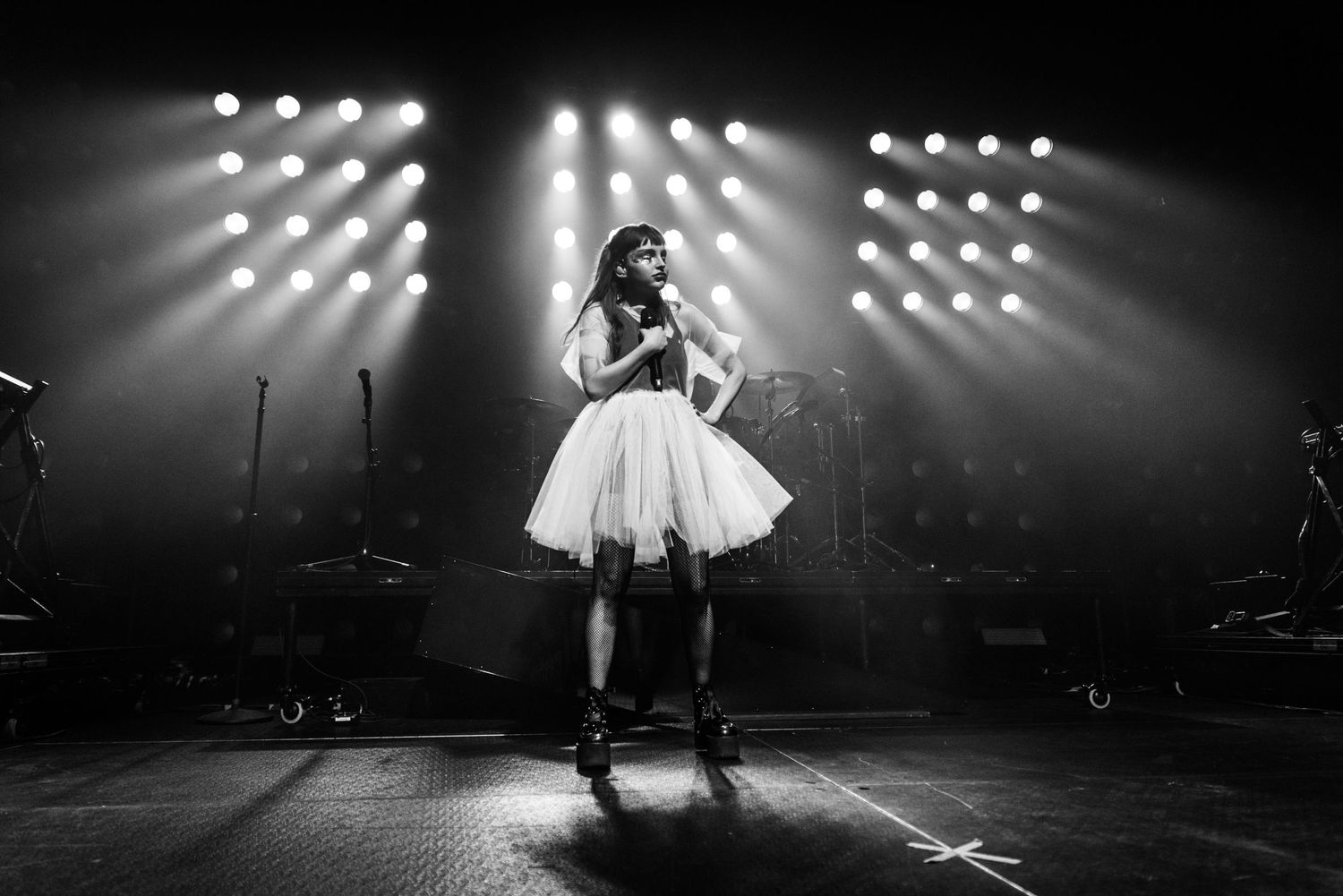 Black and white concert photo of performer in tulle dress on dramatically lit stage.