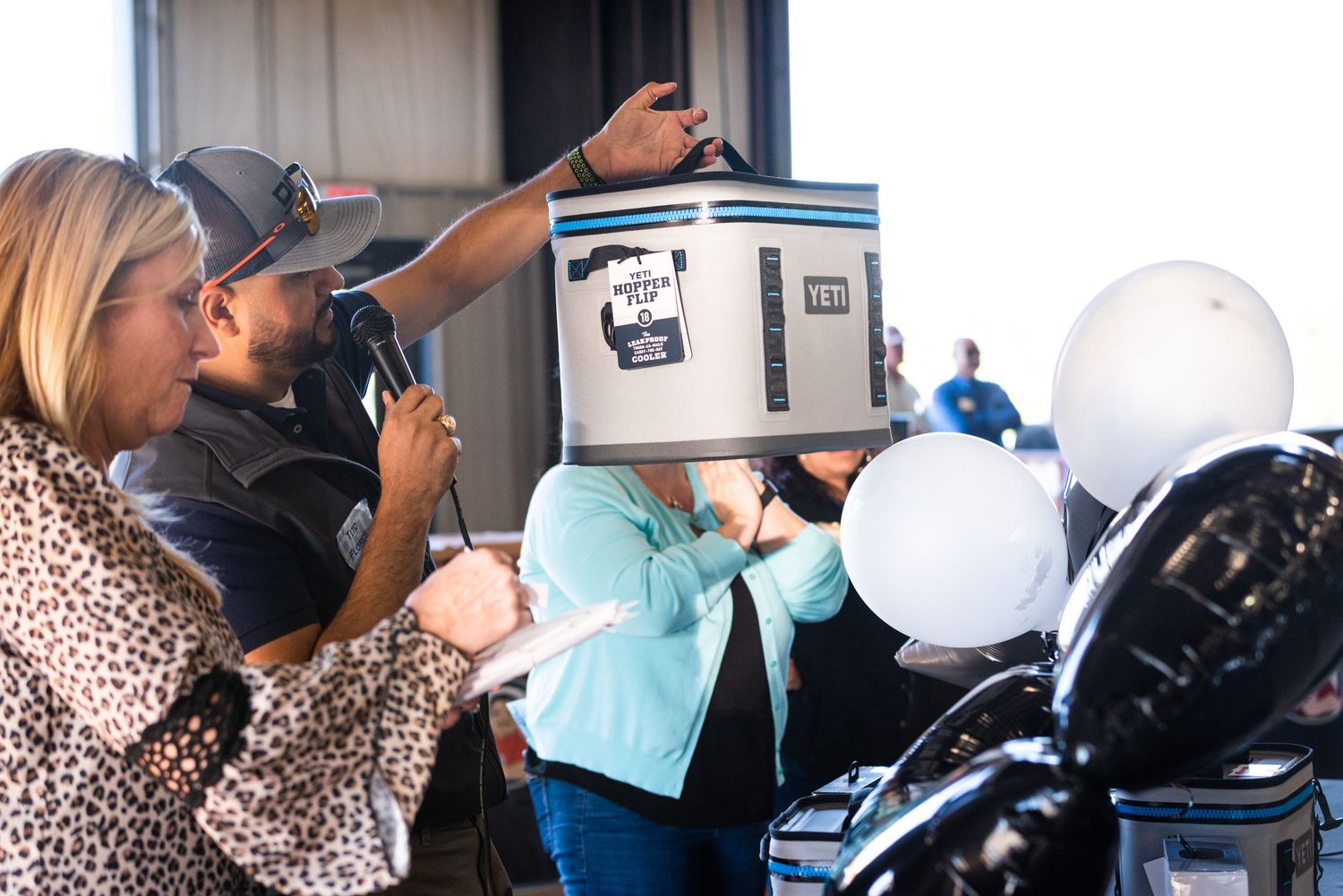 Event attendees examining YETI cooler with white balloons in background.