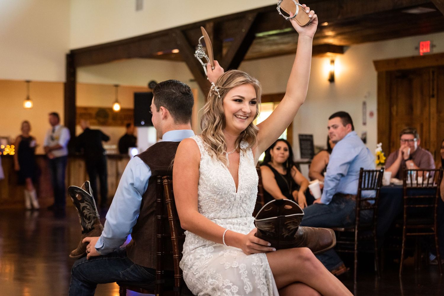 A joyful reception celebration showing people dancing in an elegant venue with wooden barn doors and rustic decor.