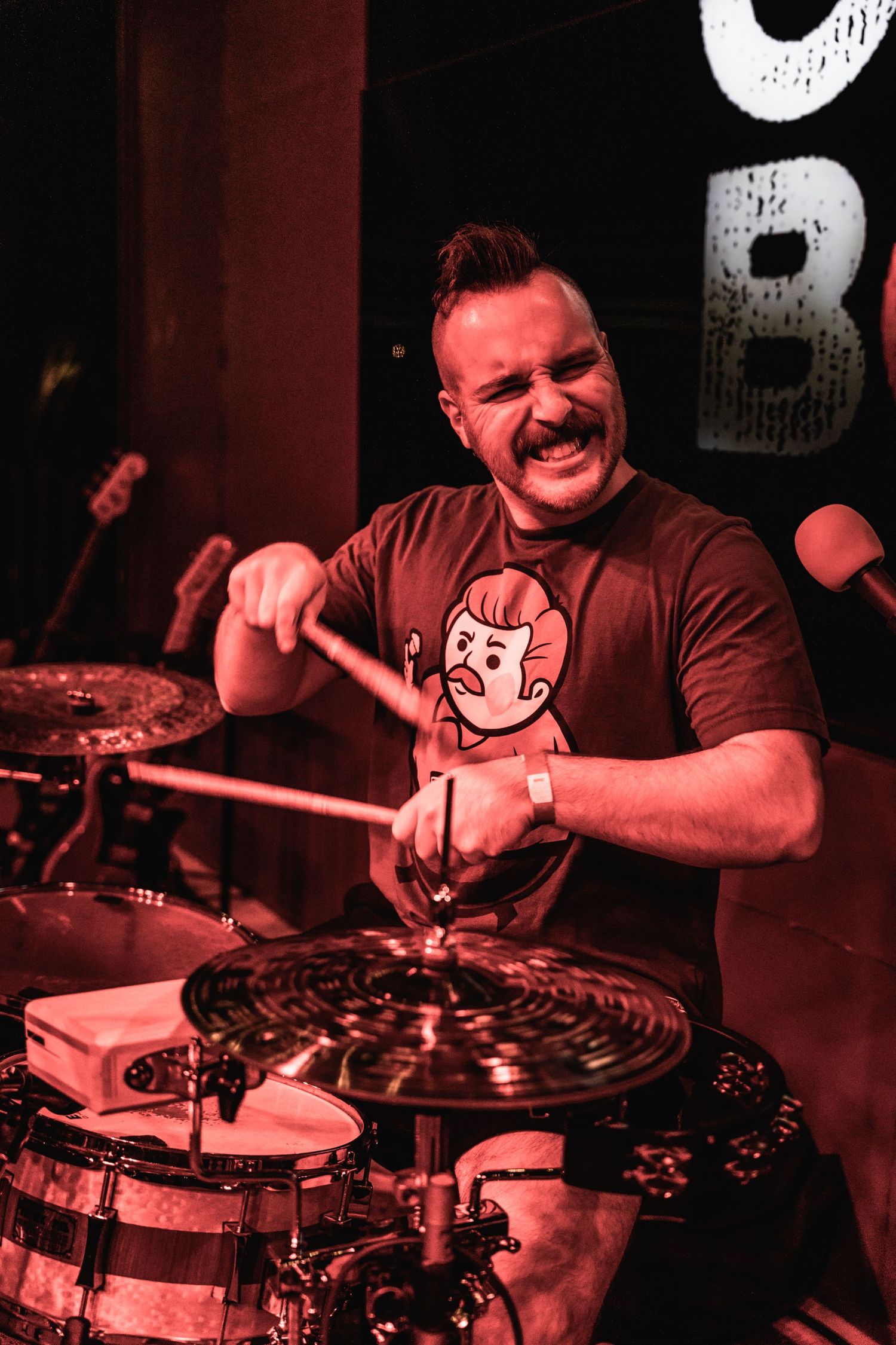 Enthusiastic drummer performs with drumsticks while wearing a brown t-shirt.