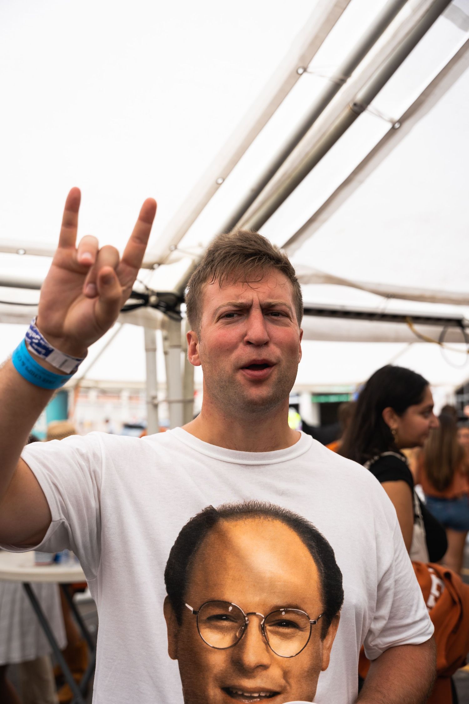 Person making peace sign while wearing t-shirt with portrait graphic at outdoor event.