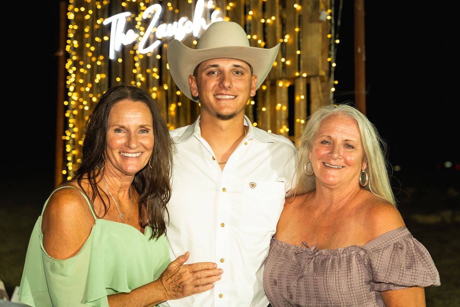 A family portrait with cowboy hat against a sparkly gold backdrop with string lights at night.