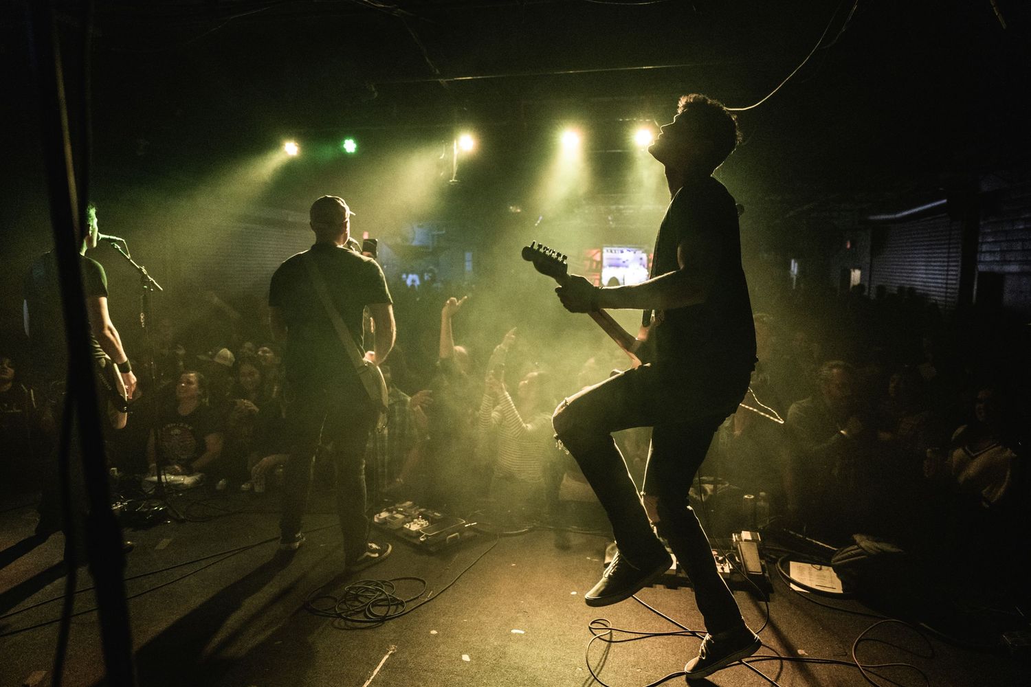 Silhouetted performers on stage with green backlighting create an atmospheric concert scene.