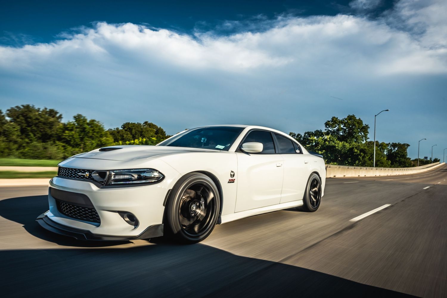 White Dodge Charger Scat Pack with custom wheels driving on sunny road.