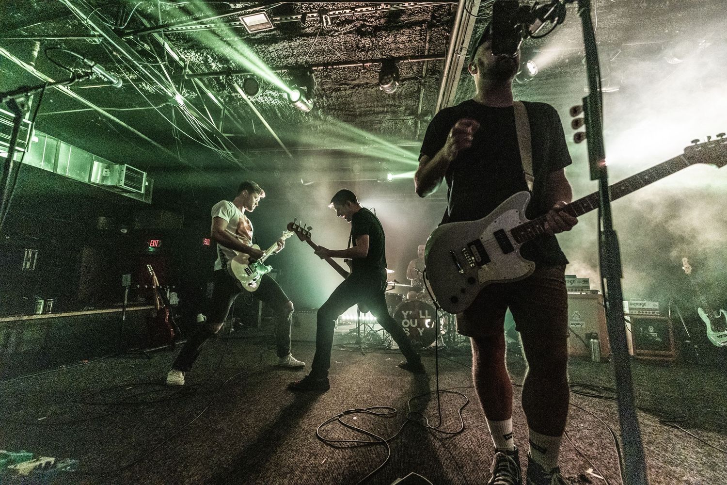 Hard rock band performs energetically on stage with green lighting and fog effects during live concert performance.
