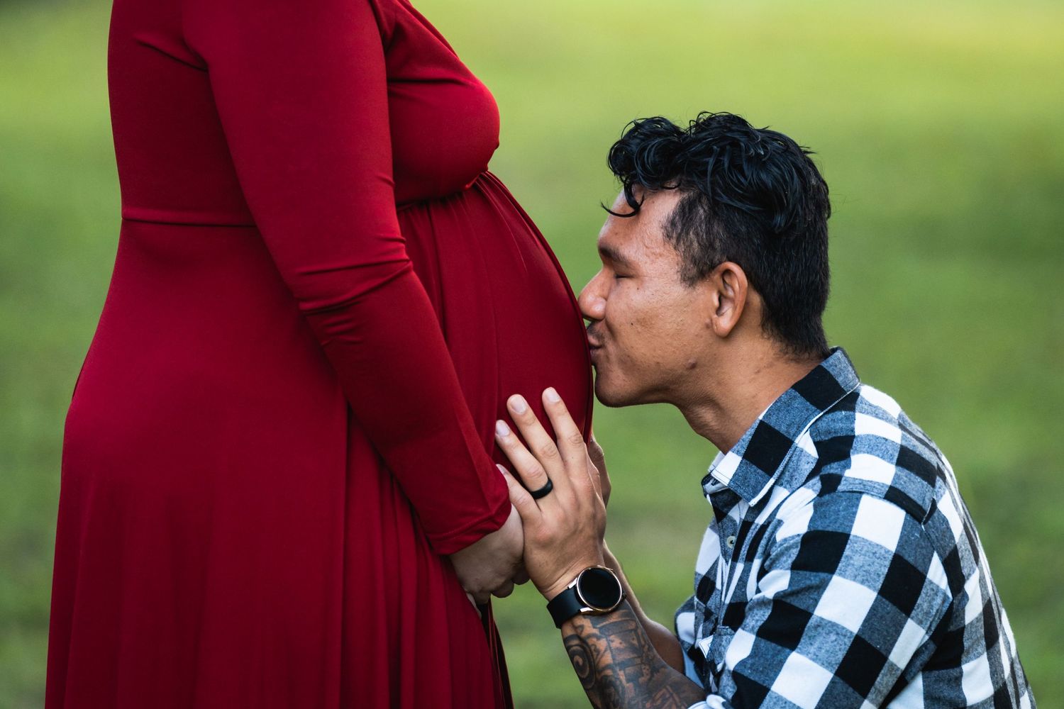 Intimate maternity moment captured outdoors with red dress and plaid shirt.
