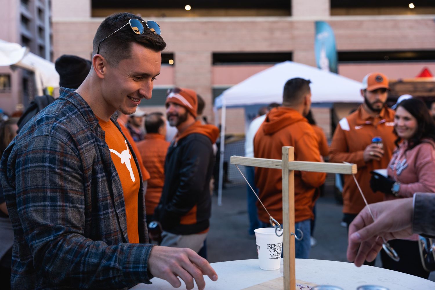 Person in plaid and orange enjoying a drink at an outdoor table during an event.