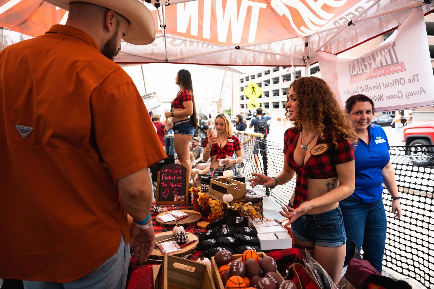 Outdoor vendor booth with drinks and merchandise under orange tent at a festival or market.