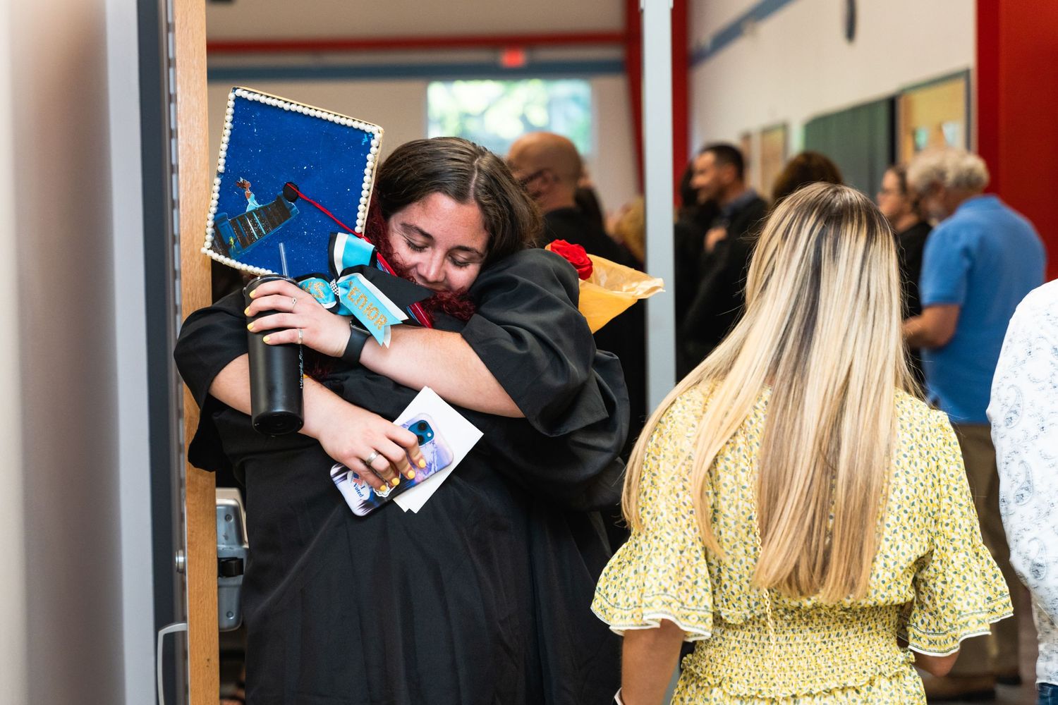 Two people share an emotional embrace at a graduation ceremony with caps and gowns.