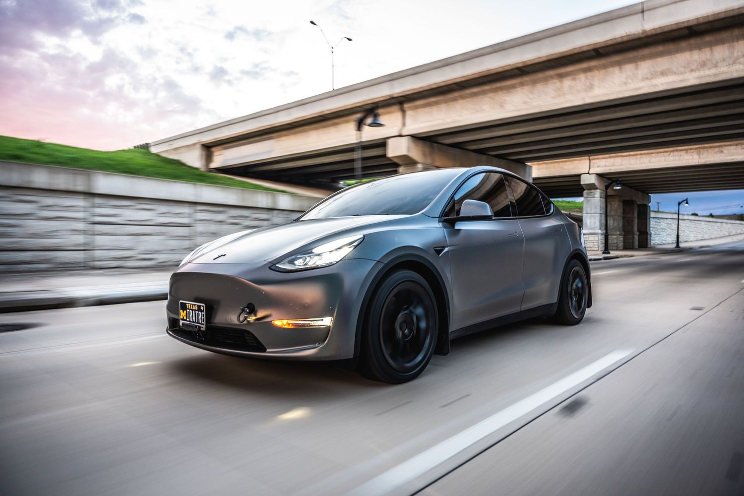 Gray Tesla Model Y with custom black wheels photographed under an overpass.